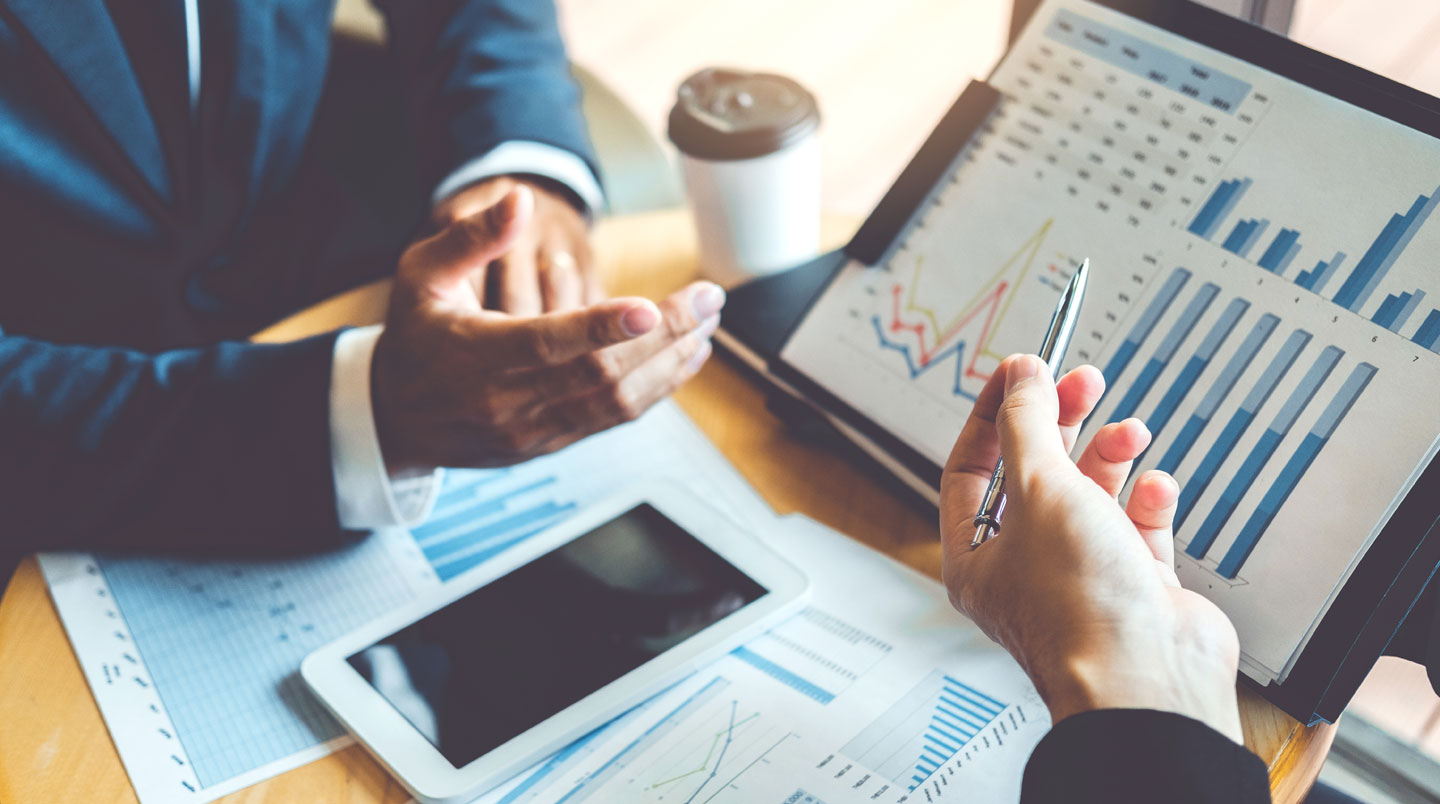 Vue de dessus d'un bureau avec documents bancaires comparatifs, ordinateur portable, smartphone et notes manuscrites illustrant le processus de décision d'un auto-entrepreneur