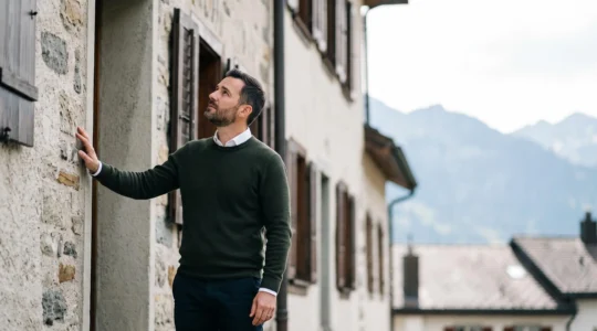 Personne évaluant attentivement la façade d'un immeuble résidentiel suisse avant un achat immobilier